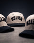 Three off-white snapback caps with black flat brims and black embroidered "WRETCH" on the front, arranged on a dark gray surface against a dark background.